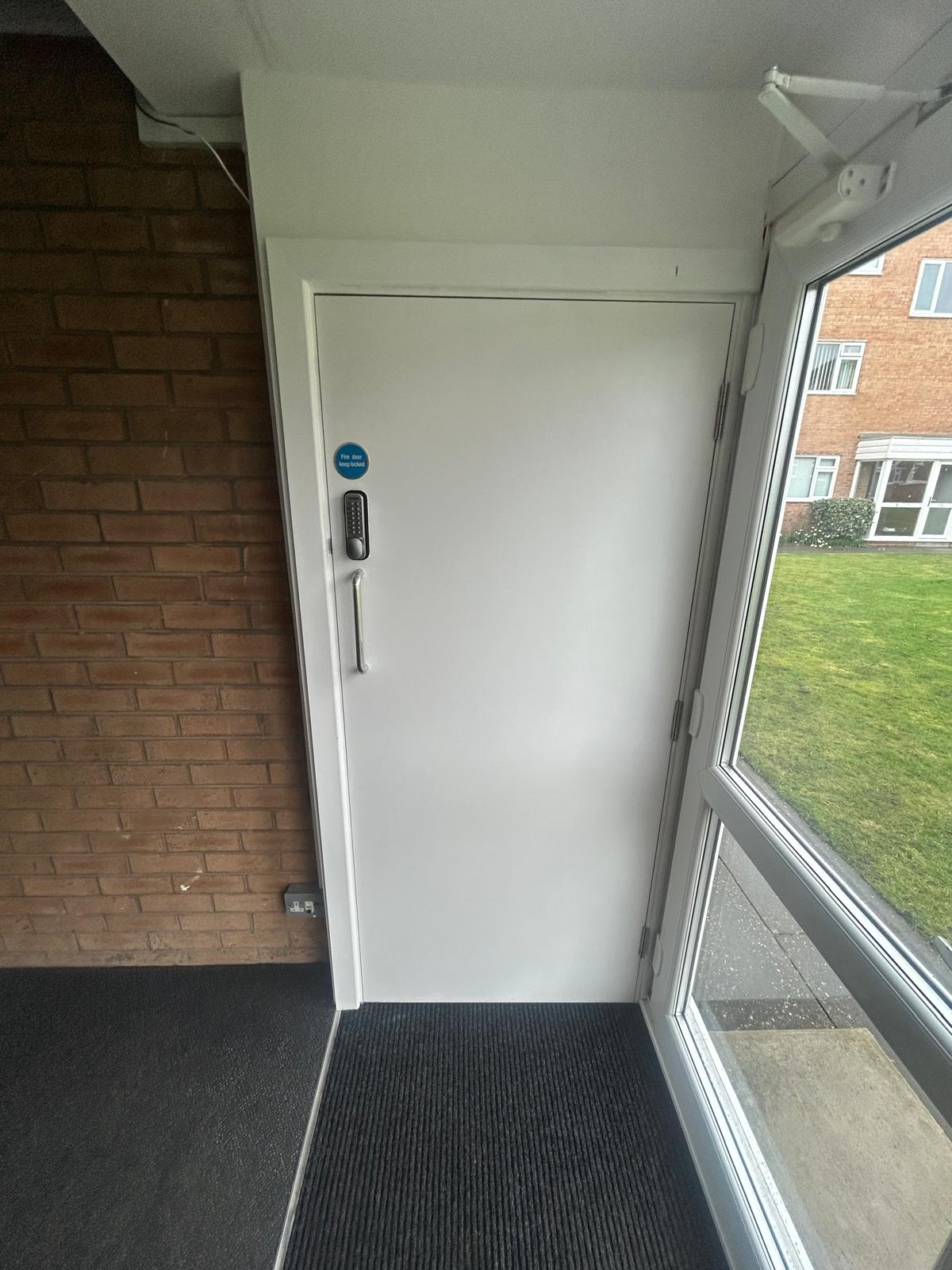 Recently maintained white FD30 fire door with keep-locked signage and overhead closer at a Liverpool communal entrance
